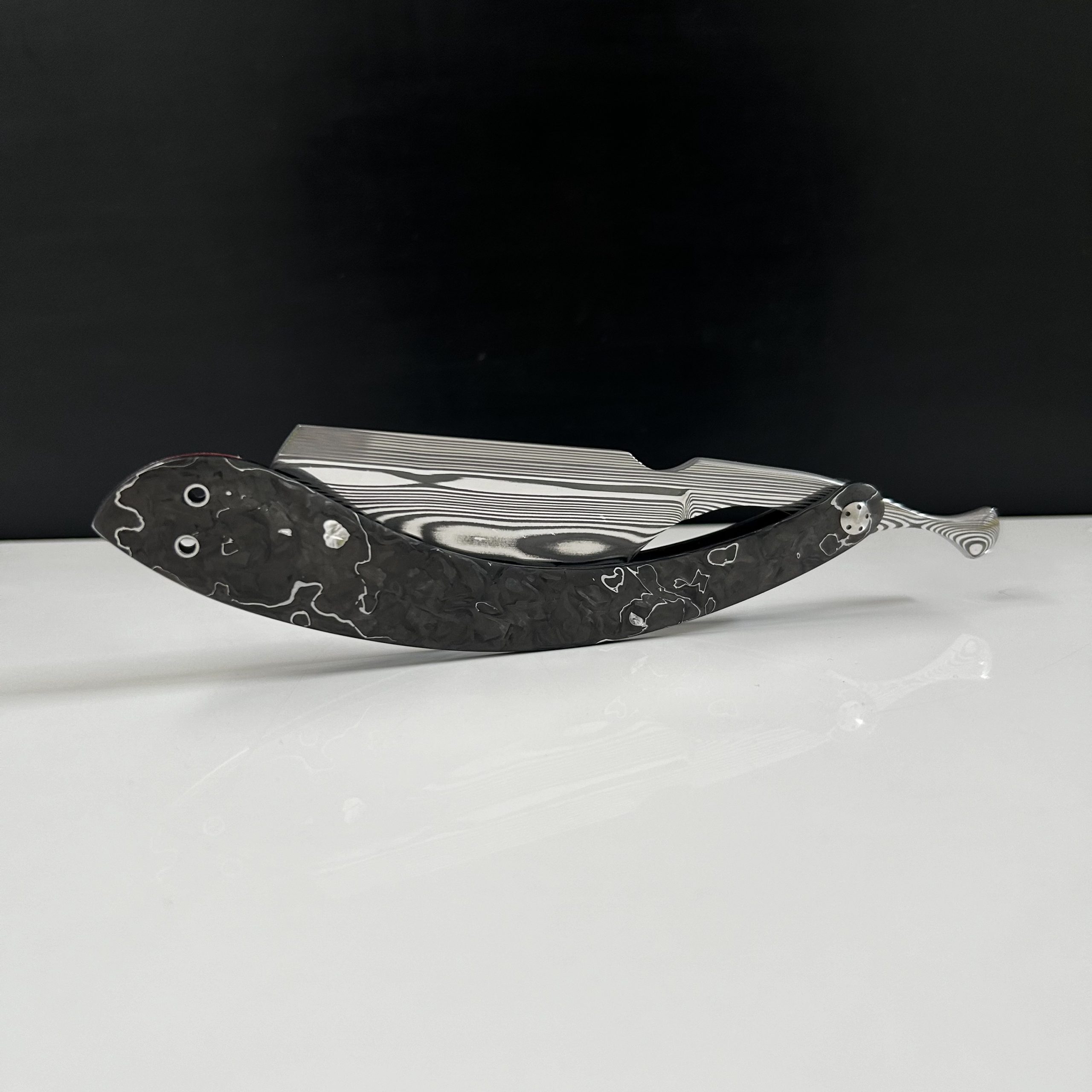 Woolfblades 390 Custom Made in a Parallel pattern Damasteel with a full hollow grind 7/8 straight edge.And the scales are made in a carbon fibre with pattern and carbon fibre inlays the wedge  on this razor is made in 25 grams of non tarnish Sterling Silver.